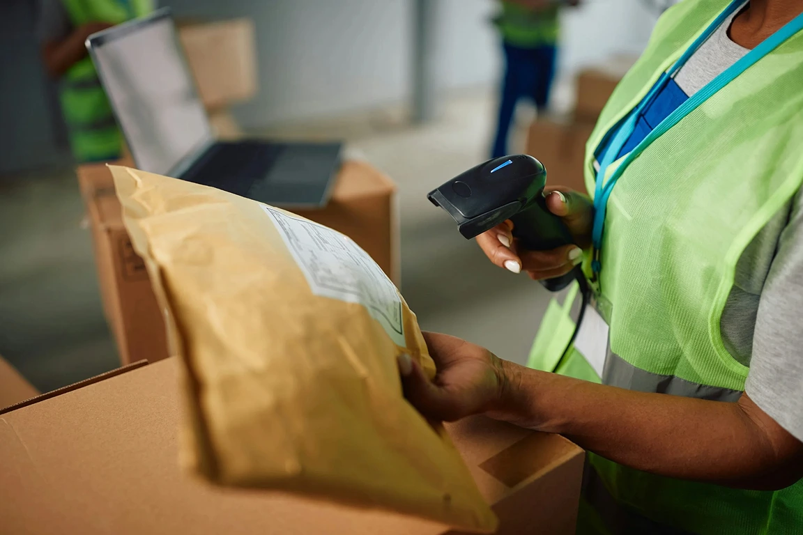 En medarbetare skannar streckkoden på ett paket med en handscanner i ett lager.